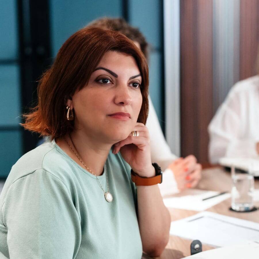 Well-dressed woman sitting at a conference table looking deep in thought.